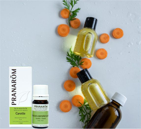 bouteille d'huile essentielle de carotte avec son emballage et quelques carottes coupées