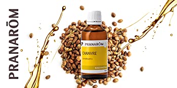 bouteille d'huile végétale de chanvre posée sur un lit de graines de chanvre avec un splash d'huile