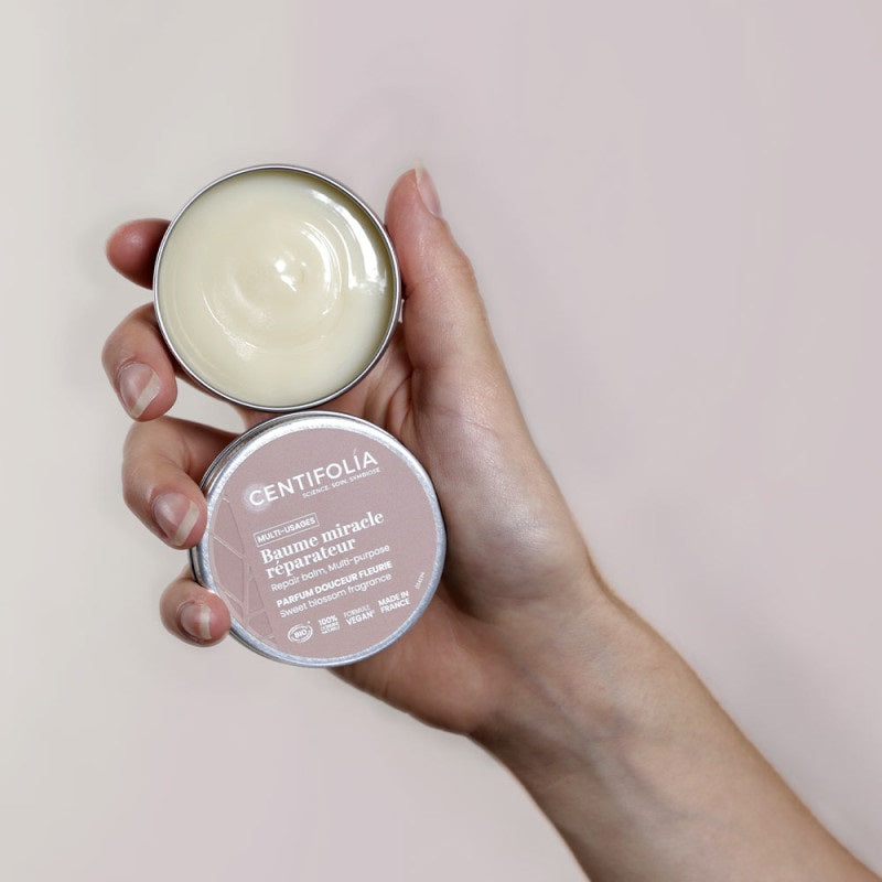 BAUME MULTI-USAGES DE MARQUE CENTIFOLIA À LA FRAGRANCE DOUCEUR FLEURIE EMBALLAGE OUVERT PRÉSENTER DANS UNE MAIN